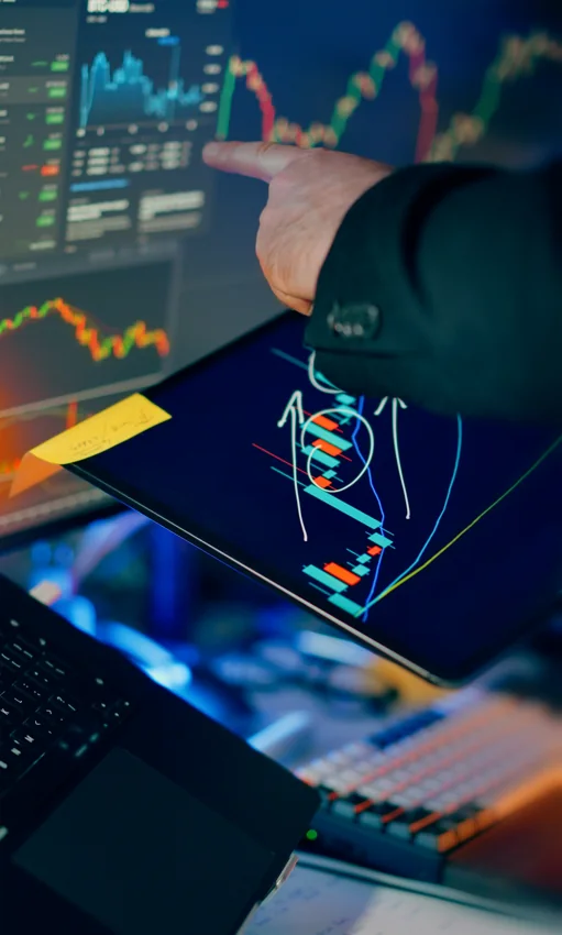 Hand pointing at a tablet that shows colorful trading charts